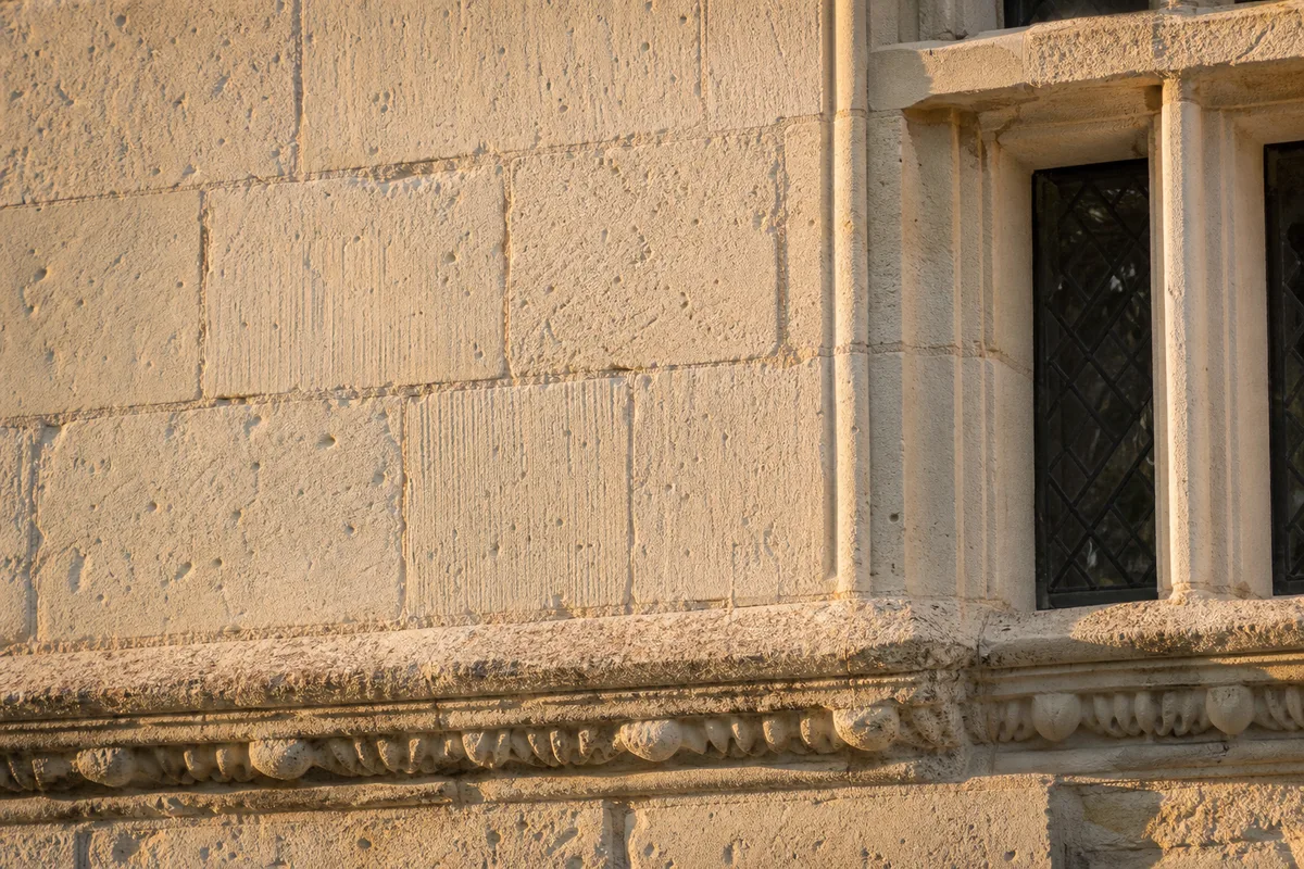 Façade de château en tuffeau blanc éclairée par une lumière rasante de fin de journée, moulures et fenêtres à meneaux visibles