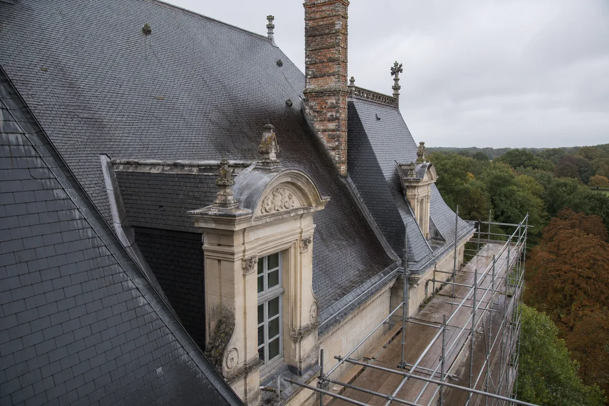 Toiture d’ardoise d’un château avec lucarnes de pierre et échafaudage de restauration